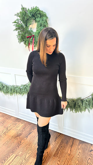 The Nikita Dress — black drop-waist sweater dress with ruffle accents